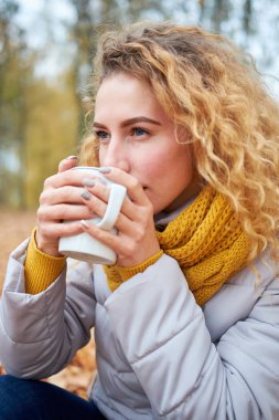 Redhead kıvırcık düşünceli kız sonbahar parkta oturup içme