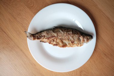 Ahşap yüzeyde beyaz tabakta kızarmış balık, yukarıdan görüş.