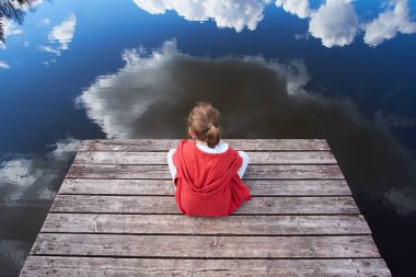 Yaz zamanı. İskelede oturan ve göle bakan kırmızı ceketli bir çocuk.