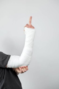 Man with plaster cast on his hand showing sing fuck you on a white wall background. Closeup view.