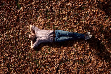 Sonbahar parkında gözleri kapalı yerde yatan çekici, neşeli genç bir adam..