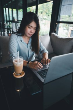 Tayland kökenli bir Asyalı kadın ofis çalışanı gün içinde bir kahve dükkanında not defterleriyle yazıp çalışıyor. Mavi bir gömlek giyiyordu.