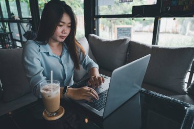 Tayland kökenli bir Asyalı kadın ofis çalışanı gün içinde bir kahve dükkanında not defterleriyle yazıp çalışıyor. Mavi bir gömlek giyiyordu.