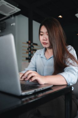 Tayland kökenli bir Asyalı kadın ofis çalışanı gün içinde bir kahve dükkanında not defterleriyle yazıp çalışıyor. Mavi bir gömlek giyiyordu.