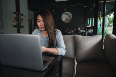 Tayland kökenli bir Asyalı kadın ofis çalışanı gün içinde bir kahve dükkanında not defterleriyle yazıp çalışıyor. Mavi bir gömlek giyiyordu.