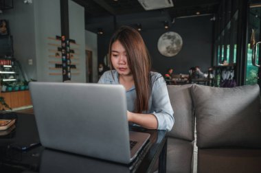 Tayland kökenli bir Asyalı kadın ofis çalışanı gün içinde bir kahve dükkanında not defterleriyle yazıp çalışıyor. Mavi bir gömlek giyiyordu.