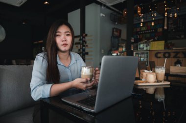 Tayland kökenli bir Asyalı kadın ofis çalışanı gün içinde bir kahve dükkanında not defterleriyle yazıp çalışıyor. Mavi bir gömlek giyiyordu.