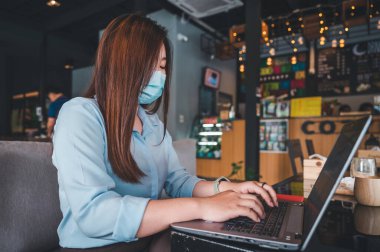 Tayland kökenli bir Asyalı kadın ofis çalışanı gün içinde bir kahve dükkanında not defterleriyle yazıp çalışıyor. Mavi bir gömlek giyiyordu.