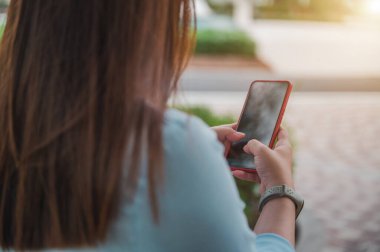 Parkta akıllı telefon kullanan bir kadın, boş bir akıllı telefon ekranı, bir insanın arkasından alınan bir bakış açısı..