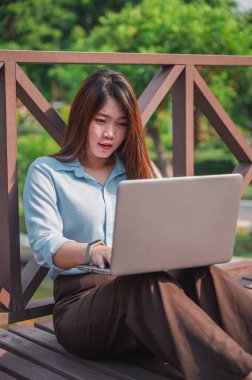 Parktaki tahta köprüde dizüstü bilgisayar kullanan kahverengi saçlı bir kadının yan görüntüsü. Genç bir ofis çalışanı gün batımında parkta yeşil çimlerin üzerinde telefonla konuşuyor..