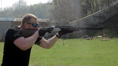 Gözlüklü bir adam hedefler ve double-barreled tüfekle vuruyor. Slowmotion