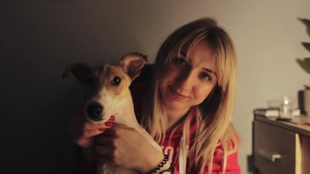 Em câmara lenta. Conforto e conceito acolhedor. Mulher muito jovem segura seu cão bonito raposa terrier em suas mãos e acariciando um cão, ela está feliz sorrindo . — Vídeo de Stock