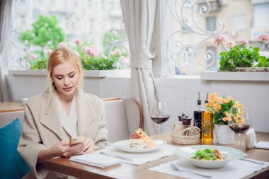 Akıllı telefon kullanan bir restoranda iş kadın. Bir muhatap için bekleyen güzel bir kadın. Beklenti