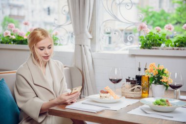 bir akşam yemeği ve cep telefonları kullanarak şehrin caddeleri üzerinde sarı saçlı Genç modeli. kadın birilerini bekliyor