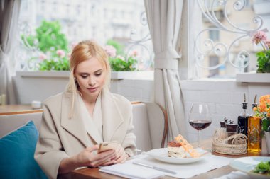 bir akşam yemeği ve cep telefonları kullanarak şehrin caddeleri üzerinde sarı saçlı Genç modeli. kadın birilerini bekliyor