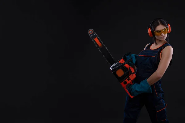 young woman with motor saw or chainsaw on a black background. gender equality. Copy space