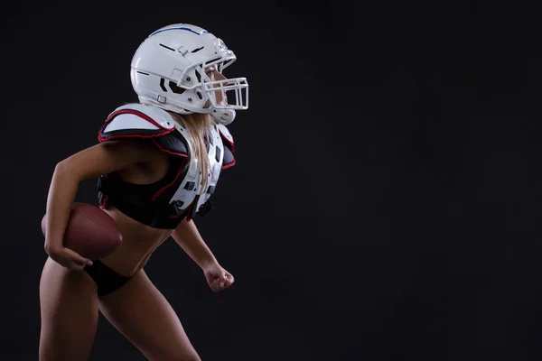 Sportive serious woman in helmet of rugby player holding ball in stuio on dark background. girl sportswoman. Gender equality. Copy space