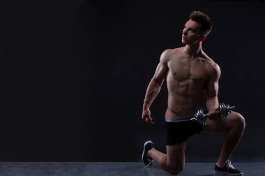 Kaslı vücut geliştirmeci adam dumbbells ile siyah arka plan üzerinde yapıyor. Kopya alanı