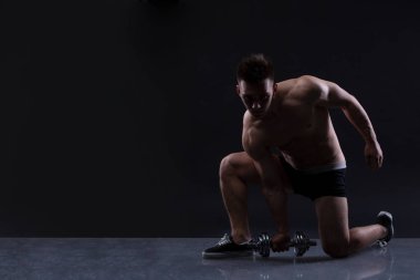 Kaslı vücut geliştirmeci adam dumbbells ile siyah arka plan üzerinde yapıyor. Kopya alanı