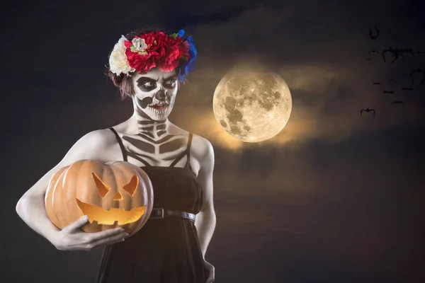 Retrato de la mujer con el esqueleto de Halloween maquillaje celebración de calabaza sobre fondo gris . — Foto de Stock