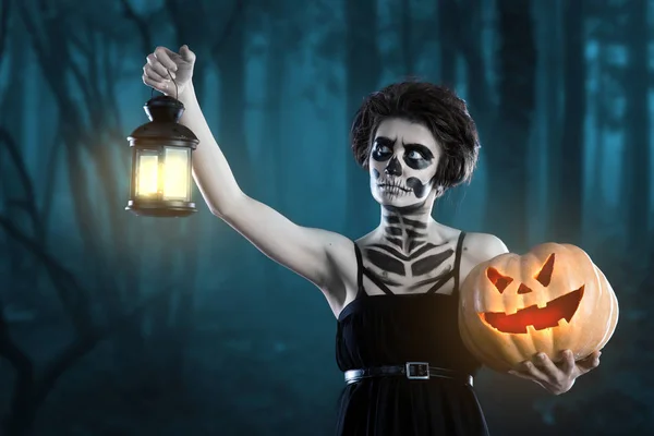 Witch with sugar skull makeup holding pumpkin at scary forest background. zombies with a lantern and a pumpkin at halloween