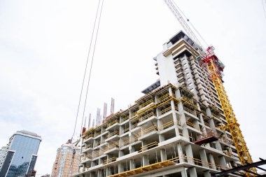 İnşaat alanı. Bitmemiş yüksek binaları ve arka planında mavi gökyüzü olan büyük endüstriyel vinçler. Darağacı. Modern inşaat mühendisliği. Çağdaş şehir manzarası.