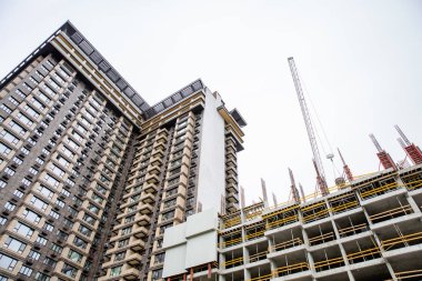 İnşaat alanı. Bitmemiş yüksek binaları ve arka planında mavi gökyüzü olan büyük endüstriyel vinçler. Darağacı. Modern inşaat mühendisliği. Çağdaş şehir manzarası.