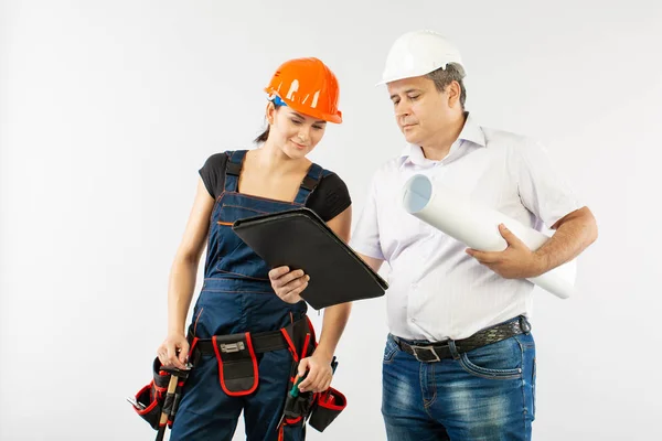 Un arquitecto con un sombrero duro o casco y una mujer constructora de compañeros de trabajo revisando planos — Foto de Stock