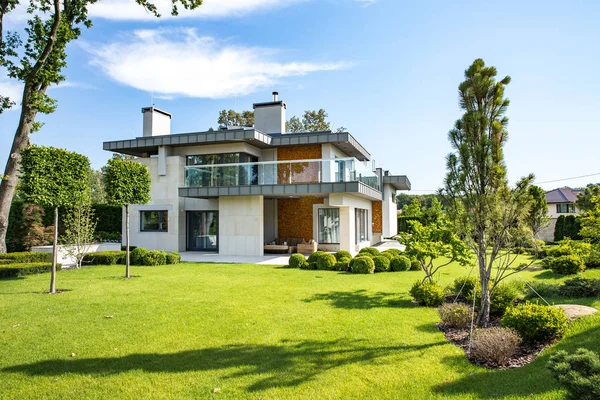 Büyük çim ve ahşap bir çit ile modern kır evi. Evin önünde bir lounge bölge ile kaplı bir teras da mevcuttur. Bahçede bir ağaç var ve çiçek. Güneşli. Dışarıda.