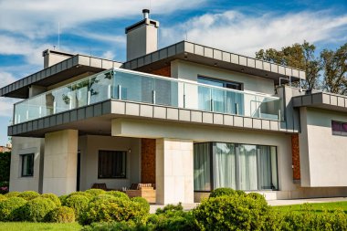 Büyük çim ve ahşap bir çit ile modern kır evi. Evin önünde bir lounge bölge ile kaplı bir teras da mevcuttur. Bahçede bir ağaç var ve çiçek. Güneşli. Dışarıda.