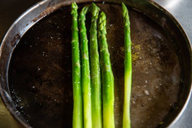 pişirme ve ızgara plaka üzerinde dumanı tüten yeşil kuşkonmaz avuç