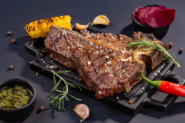 Středně propečený grilovaný Steak Ribeye Black Angus s kukuřicí a rozmarýnem na uspokojování desky blok na černém pozadí — Stock fotografie