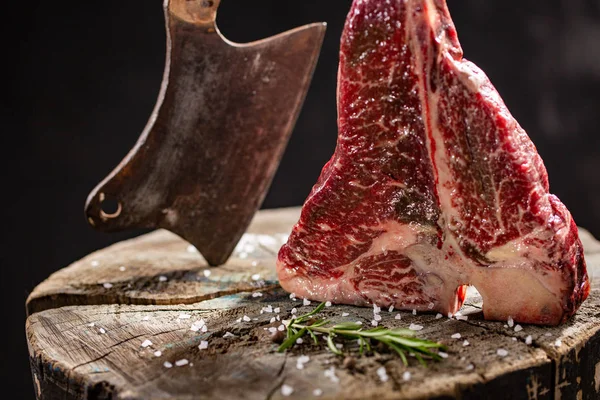 Frisches rohes T-Bones-Steak auf einem Holzbrett mit Meersalz und Küchenbeil. — Stockfoto