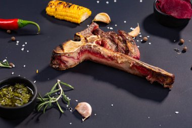 Izgara dilimlenmiş T-bone biftek ızgara mısır, sos, biber, biberiye, tuz, sarımsak siyah arka plan üzerine kümesi.