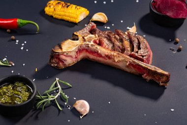 Izgara dilimlenmiş T-bone biftek ızgara mısır, sos, biber, biberiye, tuz, sarımsak siyah arka plan üzerine kümesi.