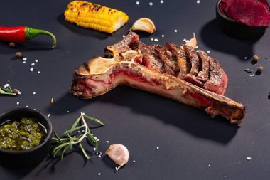 Izgara dilimlenmiş T-bone biftek ızgara mısır, sos, biber, biberiye, tuz, sarımsak siyah arka plan üzerine kümesi.