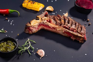 Izgara dilimlenmiş T-bone biftek ızgara mısır, sos, biber, biberiye, tuz, sarımsak siyah arka plan üzerine kümesi.
