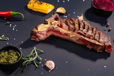 Izgara dilimlenmiş T-bone biftek ızgara mısır, sos, biber, biberiye, tuz, sarımsak siyah arka plan üzerine kümesi.