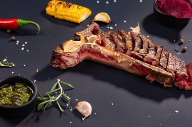 Izgara dilimlenmiş T-bone biftek ızgara mısır, sos, biber, biberiye, tuz, sarımsak siyah arka plan üzerine kümesi.