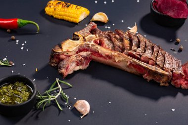 Izgara dilimlenmiş T-bone biftek ızgara mısır, sos, biber, biberiye, tuz, sarımsak siyah arka plan üzerine kümesi.