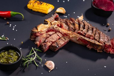 Izgara dilimlenmiş T-bone biftek ızgara mısır, sos, biber, biberiye, tuz, sarımsak siyah arka plan üzerine kümesi.