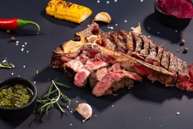Izgara dilimlenmiş T-bone biftek ızgara mısır, sos, biber, biberiye, tuz, sarımsak siyah arka plan üzerine kümesi.