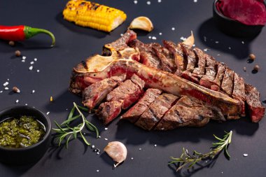 porterhouse biftek ızgara biftek ızgara mısır, sos, biber, biberiye, tuz, sarımsak siyah arka plan üzerine bir parça dilimlenmiş. rustik tarzı