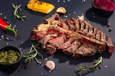porterhouse biftek ızgara biftek ızgara mısır, sos, biber, biberiye, tuz, sarımsak siyah arka plan üzerine bir parça dilimlenmiş. rustik tarzı
