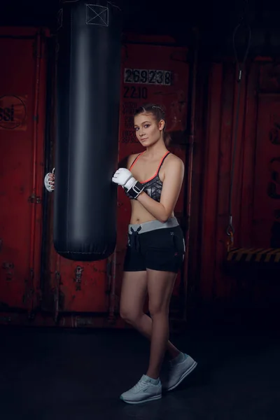 Třída, fitness. Mladé krásné sportovní žena nosí rukavice, představuje na pozadí boxu tělocvična — Stock fotografie