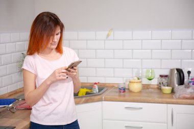 Modern ev içinde mutfak at eğilerek smartphone kullanan genç kadın. kadın telefon mesajı okuma. bir metin mesajı yazmaya Kızıl saçlı kadın