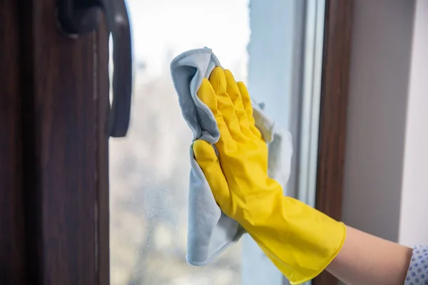 Ένα γυναικείο χέρι στα φωτεινά κίτρινα λαστιχένια γάντια πλένει. Καθαρισμός το παράθυρο με ένα μαλακό πανί. — Φωτογραφία Αρχείου