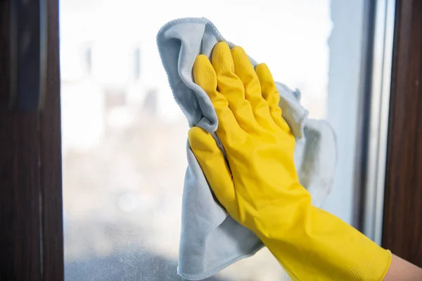 Een vrouwelijke hand in heldere gele rubberen handschoenen wast. het venster met een zachte doek schoonmaken. — Stockfoto