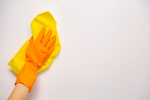 Mitarbeiter Hand in Hand mit orangefarbenem Gummischutzhandschuh wischt weiße Wand mit gelbem trockenen Lappen vom Staub. allgemeine oder regelmäßige Säuberung. Gewerbliche Reinigungsfirma. Kopierraum. — Stockfoto