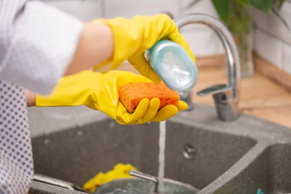 Huisvrouw in rubber gekleurde handschoenen afwassen met oranje spons in de keuken thuis. — Stockfoto